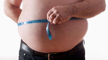 A fat man measuring his stomach with a tape measure