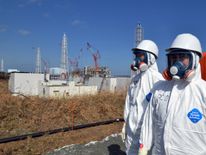 Workers stand on front of the Fukushima power plant months after a meltdown at the site