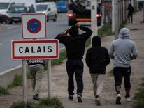 Migrants living in the 'Jungle' migrant camp walk past a sign posted along a road that leads to the town of Calais in northwestern France on September 26, 2016, French President Francois Hollande said on a visit to the port of Calais that the sprawling 'Jungle' migrant camp would be 'definitively dismantled' under a plan to relocate the migrants to centres around the country. / AFP / DENIS CHARLET (Photo credit should read DENIS CHARLET/AFP/Getty Images)