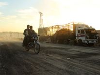 Men drive a motorcycle near a damaged aid truck