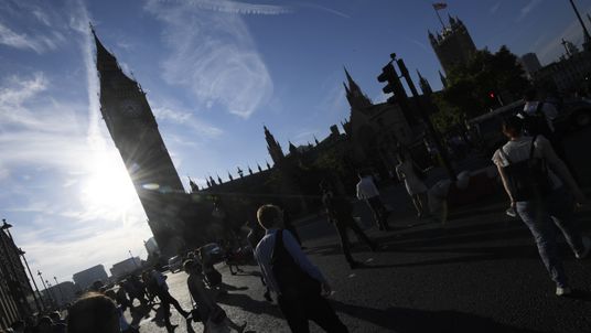 Pedestrians cross the road as the sun rises behind Big Ben earlier today
