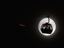 The moon rises behind clouds as the Emirates Air Line cable car is pictured in London