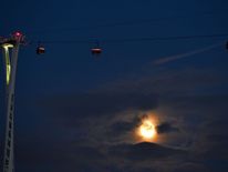 The moon rises behind clouds as the Emirates Air Line cable car is pictured in London