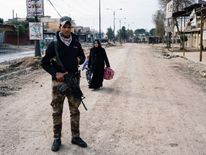 An Iraqi special forces Counter Terrorism Service (CTS) member stands guard in a street in Mosul's al-Zahraa neighborhood on January 8, 2017, as a woman and her child flee during an ongoing military operation against Islamic State (IS) group militants. Elite Iraqi forces battling the Islamic State group in eastern Mosul reached the Tigris River that splits the city in two for the first time, a spokesman said