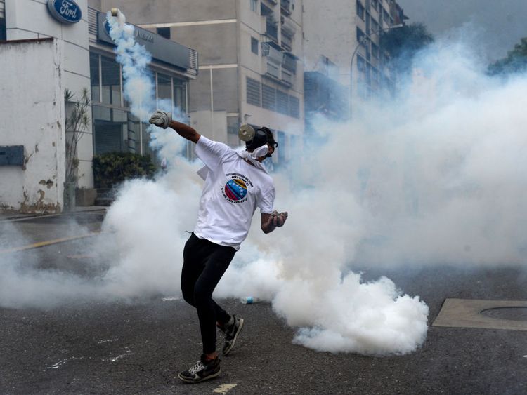 A demonstrator throws a tear gas grenade back at police during a march against Mr Maduro