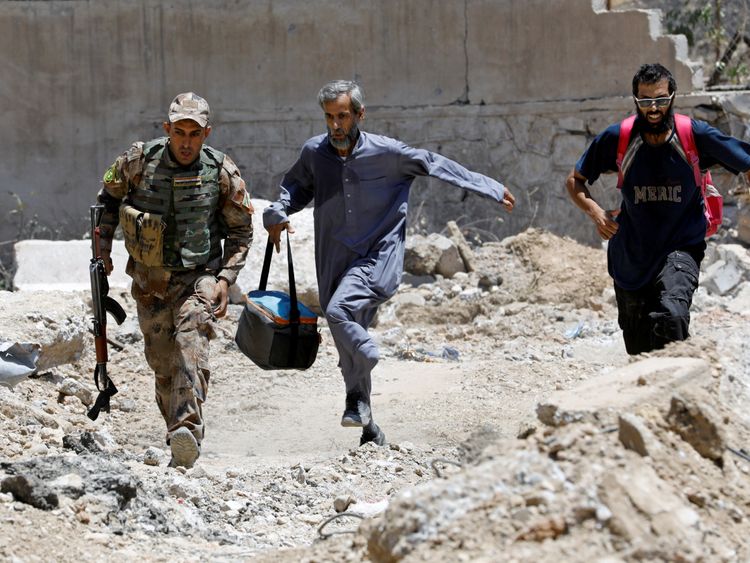 An Iraqi soldier and civilians run to avoid snipers of the Islamic State militants