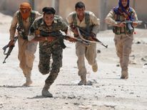 Os lutadores curdos das Unidades de Proteção das Pessoas (YPG) atravessam uma rua em Raqqa