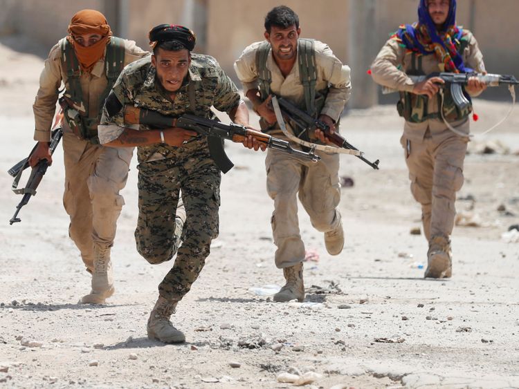 Os lutadores curdos das Unidades de Proteção das Pessoas (YPG) atravessam uma rua em Raqqa