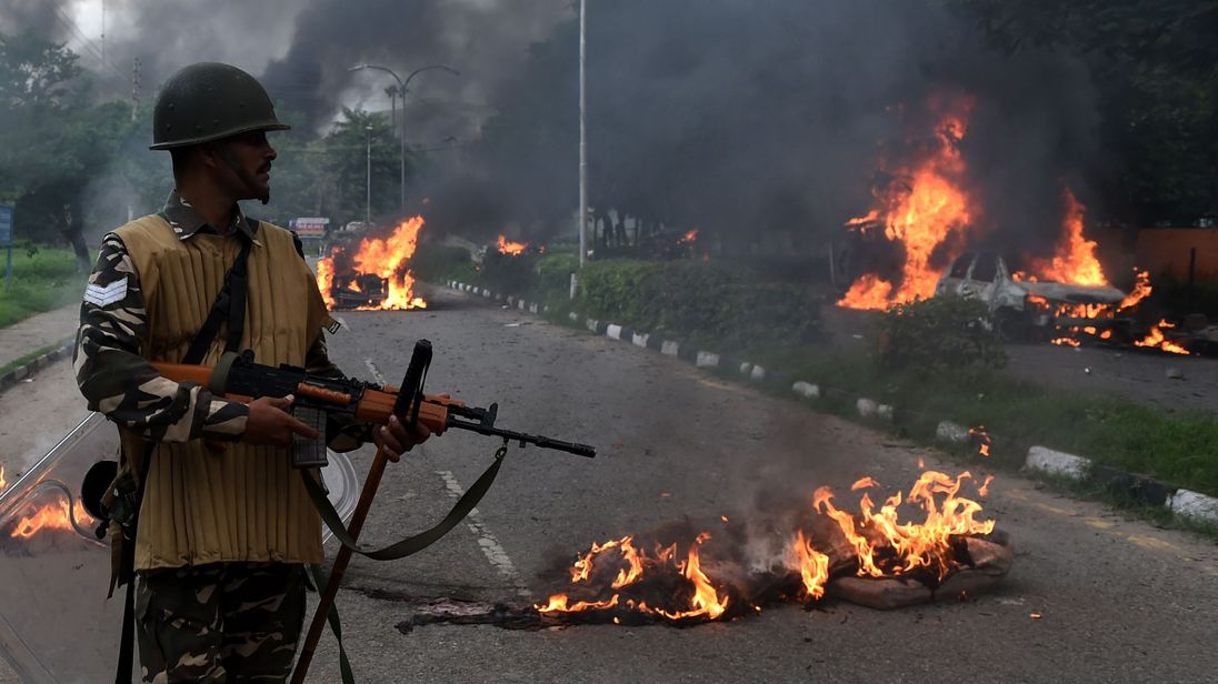 Indian security personnel looks at burning vehicles set alight by rioting followers of a religious leader convicted of rape