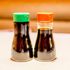 Two soy sauce bottles on the table. One is considered low sodium and has a green top, the other is considered high (or normal) sodium which has a red top.