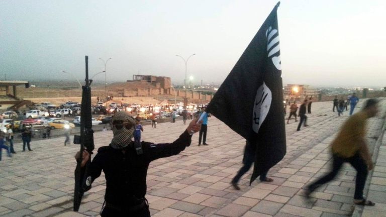 A fighter of the ISIL/ISIS holds a flag and a weapon on a street in Mosul, Iraq