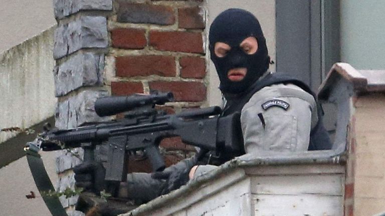 A masked Belgian policeman secures the area from a rooftop near the scene where shots were fired during a police search of a house in the suburb of Forest near Brussels