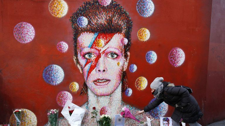 Eine Frau hinterlässt einen Blumenstrauß an einem Wandbild von David Bowie in Brixton im Süden Londons