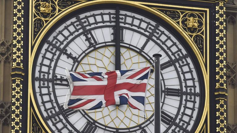 A British Union flag flutters in front of one of the clock faces of the 'Big Ben' clocktower of The Houses of Parliament in central London