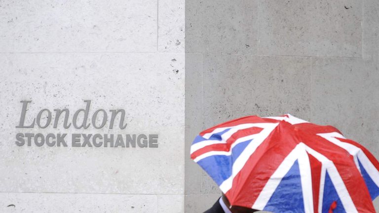 A worker shelters from the rain as he passes the London Stock Exchange in the City of London