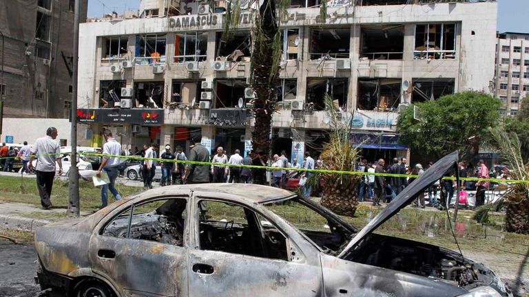 A destroyed car is pictured near a damaged building after a blast at Marjeh Square in Damascus