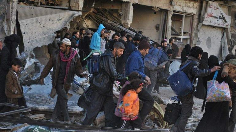 Syrian civilians walk as they are evacuated during a humanitarian operation in the besieged Syrian city of Homs