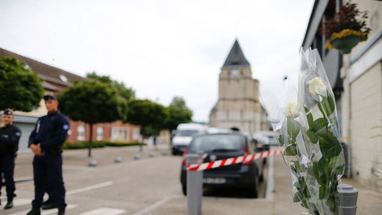 Flowers laid in tribute to Father Jacques Hamel as police officers stand guard the street to the Saint-Etienne church.