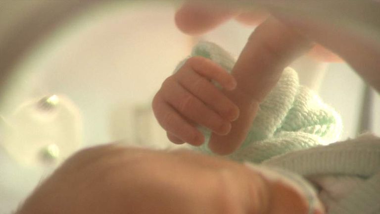 A newborn baby holding an adult's finger