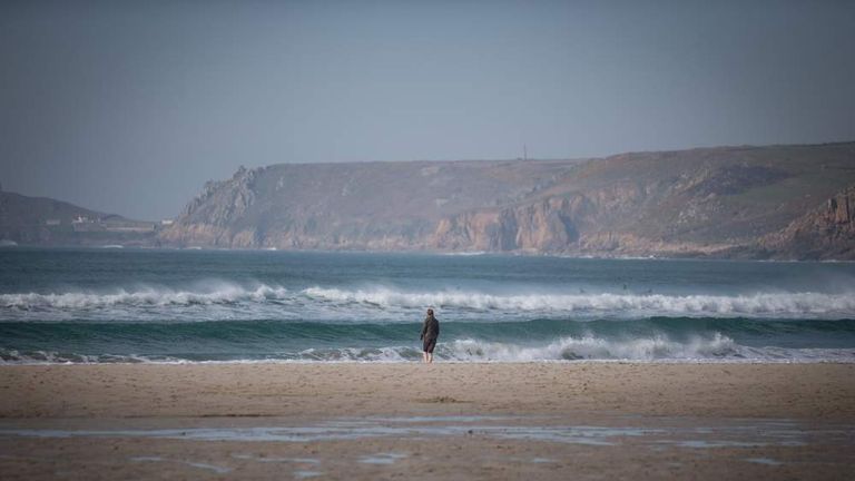 A walker looks at breaking waves in Sennen Cove