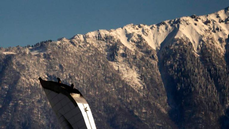 Workers stand atop of the Olympic torch in front of Caucasus Mountain at the Olympic Park in the Adler district of Sochi