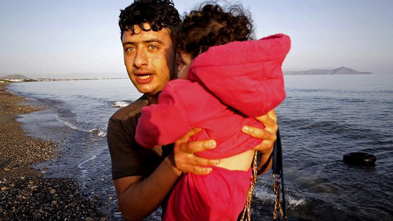A Syrian refugee holds a toddler as he jumps off a dingy boat on Kos after crossing part of the Aegean Sea from Turkey to Greece