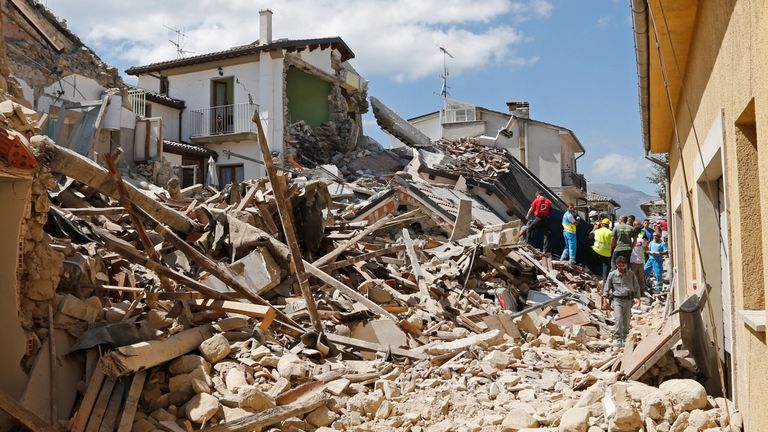 People and rescuers stand next collapsed buildings following an earthquake in Amatrice, central Italy