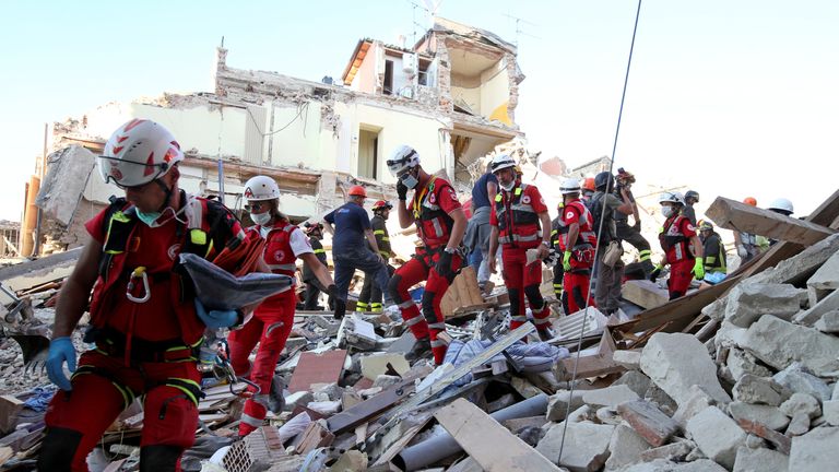 Rescuers walk through rubble following the earthquake in Amatrice,