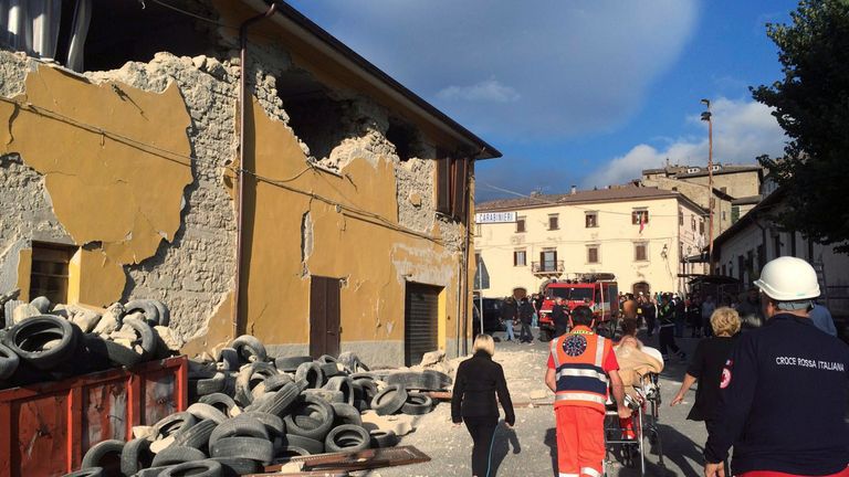Rescuers and people walk along a road in Accumoli di Rieti, central Italy