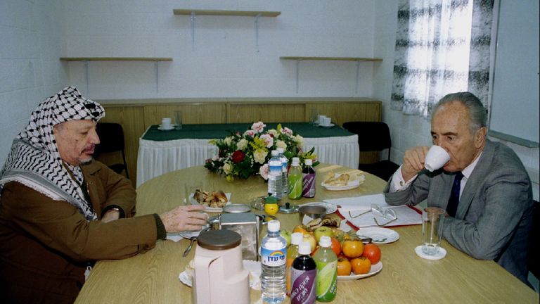 Israeli Foreign Minister Shimon Peres drinks as PLO chairman Yasser Arafat reaches for a pen during a private meeting 9 January 1995