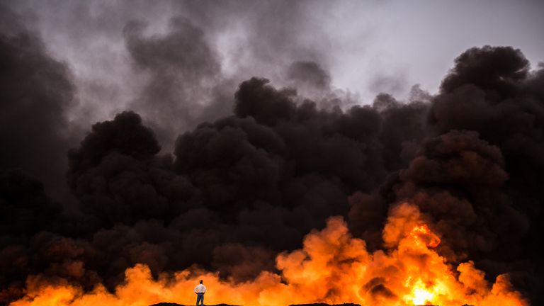 A man stands in front of a fire from oil that has been set ablaze in the Qayyarah area