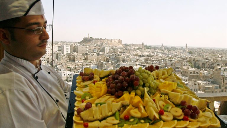 A chef displays a collection of dessert fruits with the historic city of Aleppo in the background October 21, 2007