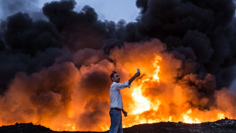 A man takes a selfie in front of a fire from oil that has been set ablaze in the Qayyarah area