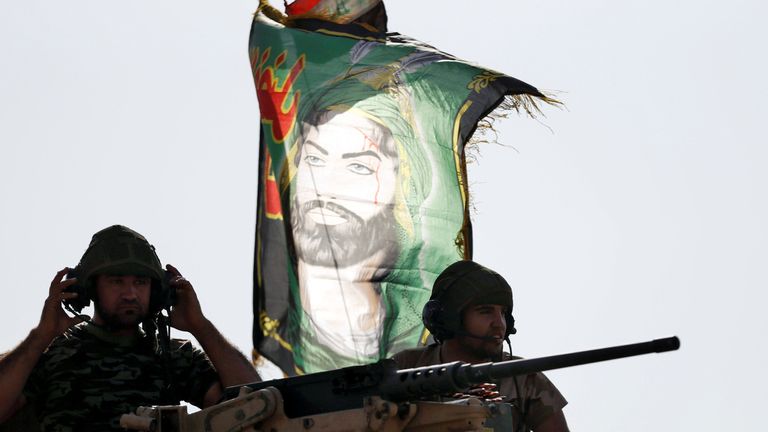Iraqi special forces soldiers sit on top of an armoured vehicle next to a flag of Imam Hussein in Bartella