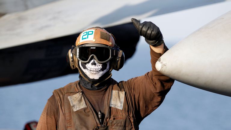 A flight deck crew member stands next to an F/A-18E Super Hornet just before take off for Mosul, Iraq to provide air-support 