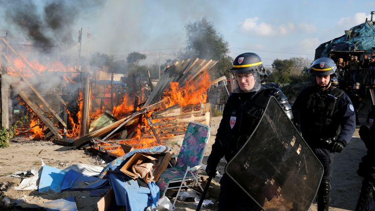 French riot police officer secures the area near a burning makeshift shelter set ablaze in protest against the dismantlement of the camp for migrants called the "Jungle" in Calais on the second day of their evacuation and transfer to reception centers, France, October 25, 2016. REUTERS/Pascal Rossignol