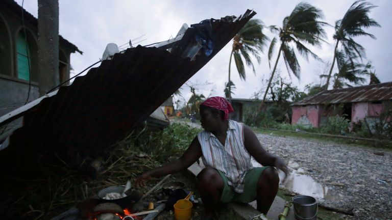 A woman cooks next to a house damaged by Hurricane Matthew in Les Cayes, Haiti
