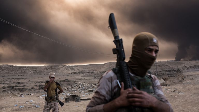 Iraqi soldiers look on as smoke rises from the Qayyarah area