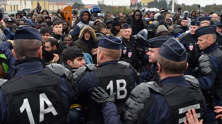 French riot police officers hold back migrants