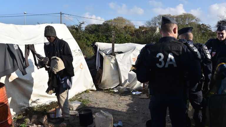 French riot police look on as a migrant in the camp gathers his belongings