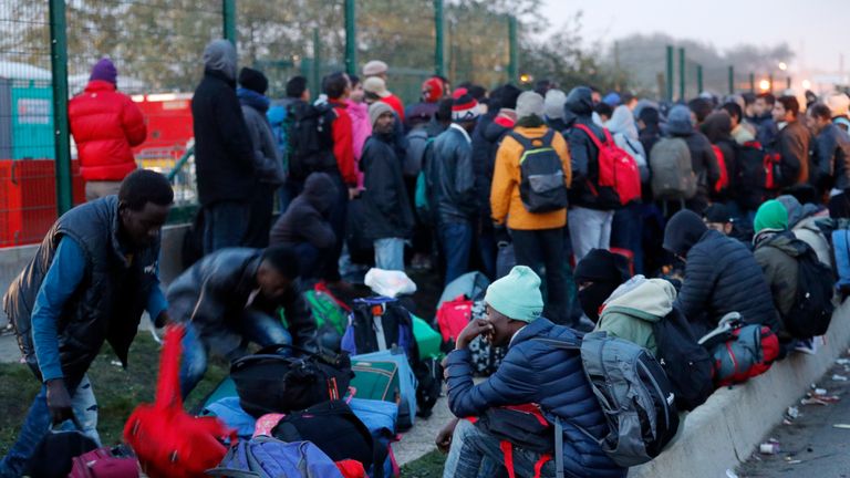 Migrants wait in front of a processing centre on the second day of their evacuation and transfer to reception centres in France