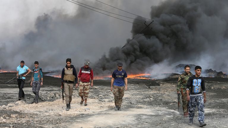 Tribal fighters walk near burning oil wells in Qayyara