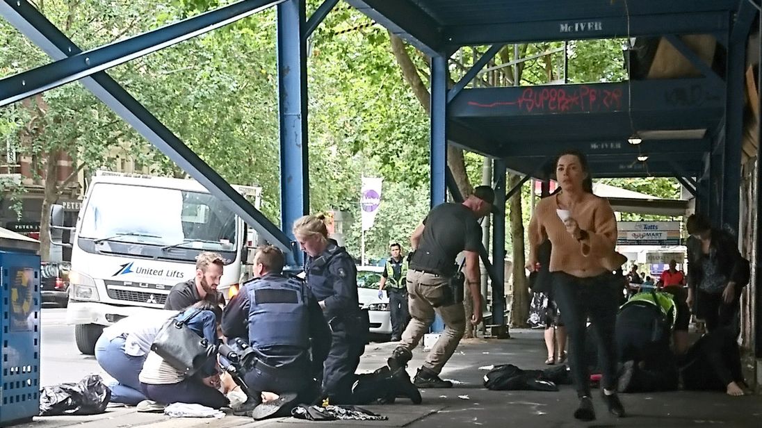 Members of the public watch as police and emergency services attend to an injured person after a car hit pedestrians in central Melbourne Australia