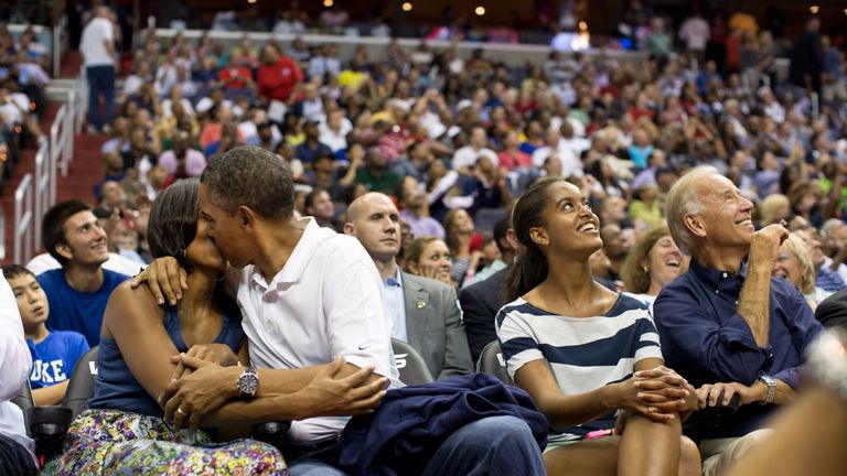 Barack Obama kisses his wife Michelle at a basketball game next to daughter Malia and Vice President Joe Biden