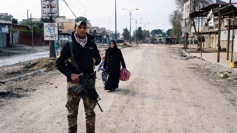 An Iraqi special forces Counter Terrorism Service (CTS) member stands guard in a street in Mosul&#39;s al-Zahraa neighborhood on January 8, 2017, as a woman and her child flee during an ongoing military operation against Islamic State (IS) group militants. Elite Iraqi forces battling the Islamic State group in eastern Mosul reached the Tigris River that splits the city in two for the first time, a spokesman said