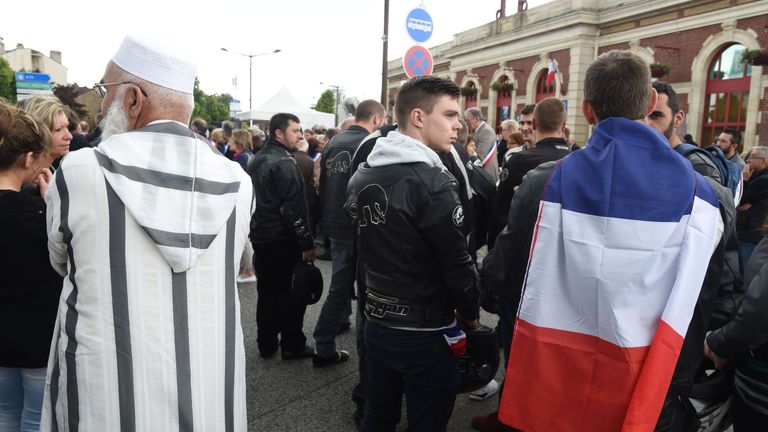 A man wearing a French flag stands next to a man wearing a Muslim clothing as people gather outside the railway station in Mantes-la-Jolie on June 18, 2016, to take part in a march in tribute to French policeman Jean-Baptiste Salvaing and his partner Jessica Schneider who were killed outside their home in Magnanville, by a convicted extremist who had pledged allegiance to the Islamic State group