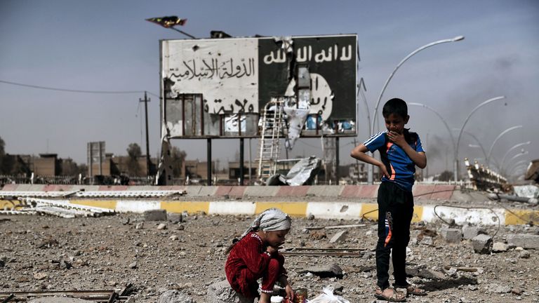Iraqi children sit amidst the rubble of a street in Mosul's Nablus neighbourhood infront of a billboard bearing the logo of the Islamic State (IS) group