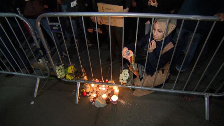 A woman wearing a headscarf lights a candle at one of the memorials set up at the vigil