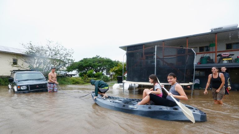 People paddle in a kayak after flood waters entered their back yard in Murwillumbah