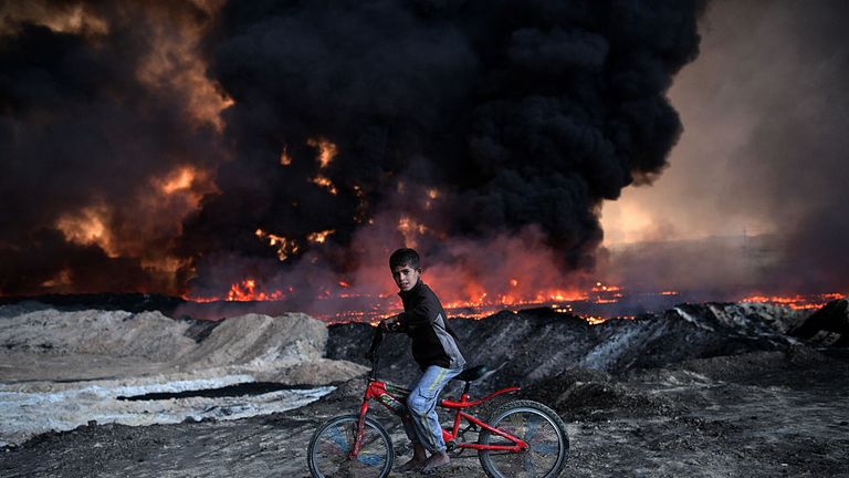 A boy rides his bike past an oil field set on fire by retreating IS fighters